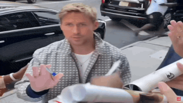 a man in a grey jacket is signing autographs on the sidewalk