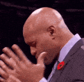 a bald man in a suit with a red poppy on his lapel is clapping his hands