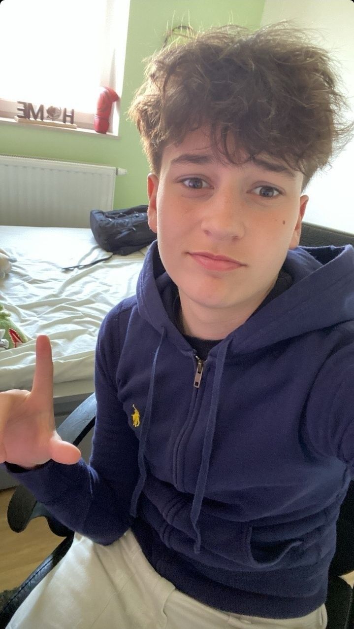 This may contain: a young boy sitting on top of a bed giving the peace sign with his hand