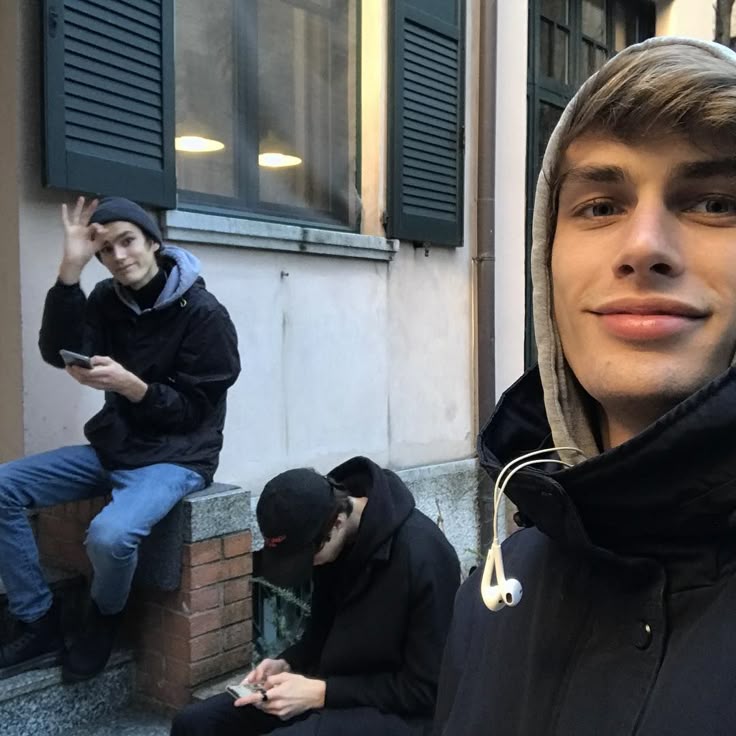 This may contain: two men sitting on the steps in front of a building and one is holding his cell phone