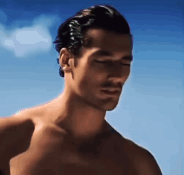 a shirtless man with his eyes closed is standing on a beach .