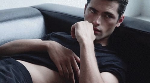 a man in a black shirt is laying on a black couch with his hand on his chin