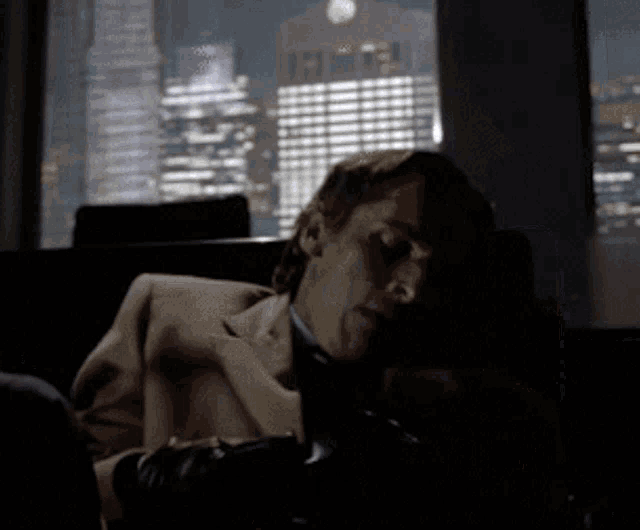 a man in a suit and tie is sleeping on a couch in front of a window