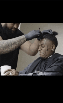 a man getting his hair cut by a man with a tattoo on his arm