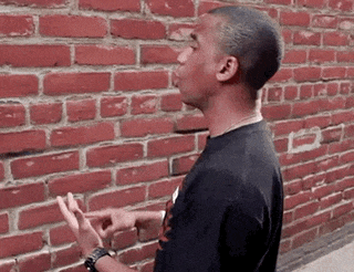 a man in a black shirt is standing in front of a red brick wall .