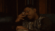 a man is sitting on a couch smoking a cigarette and holding his hand to his forehead .