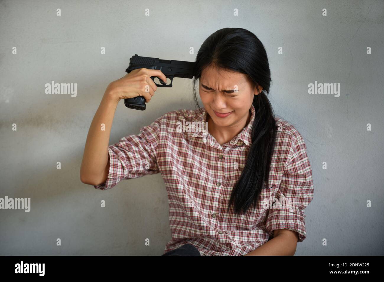 depressed-young-woman-holding-gun-on-head-against-wall-2DNW225.jpg
