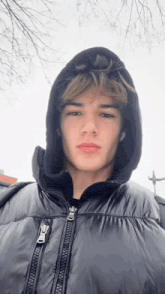 a young man wearing a black jacket with a hood is standing in the rain .