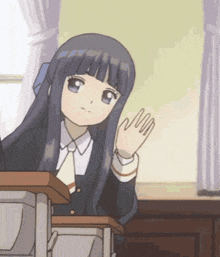 a girl is sitting at a desk waving her hand