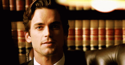 a man in a suit and tie is sitting in front of a bookshelf with books .