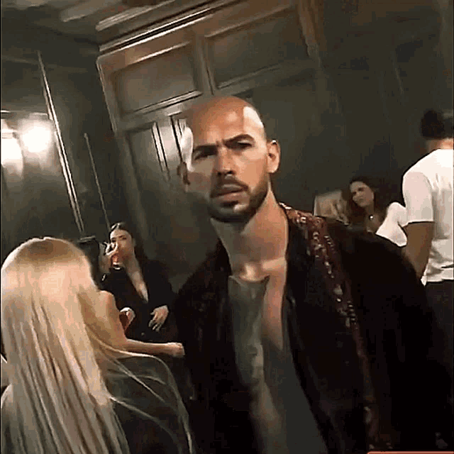 a bald man with a beard is standing in a crowd of people in a dark room .