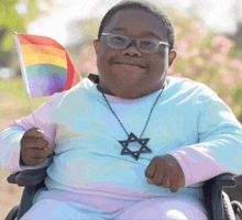 a young boy in a wheelchair holds a small rainbow flag