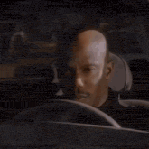 a man with a bald head is driving a car and looking at the camera