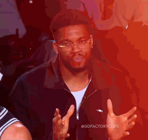 a man wearing glasses and a black jacket is making a funny face with his hands outstretched .