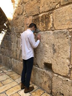 This may contain: a man standing next to a stone wall talking on a cell phone