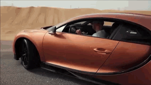 a man is driving a bugatti chiron car on a desert road