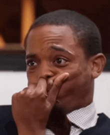 a man in a suit and tie is covering his face with his hand .