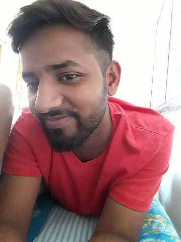 image-of-young-happy-smiling-handsome-indian-man-in-early-20s-lying-on-bed-wearing-red-v-neck.jpg