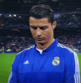 a man wearing a blue adidas jacket is standing on a soccer field