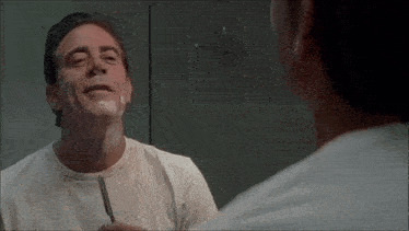 a man is shaving his face in front of a bathroom mirror