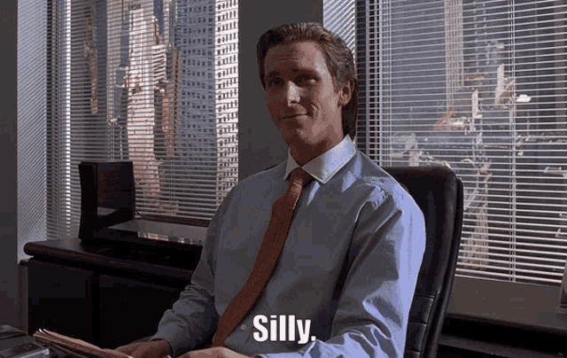 a man in a blue shirt and red tie is sitting in front of a window and says silly
