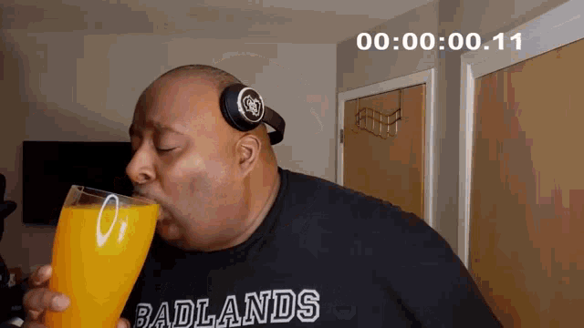 a man wearing headphones and a shirt that says badlands drinks a glass of orange juice