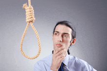 a man holds his hand to his chin while looking at a noose hanging from a rope