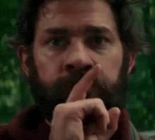a close up of a man with a beard holding his finger to his lips .