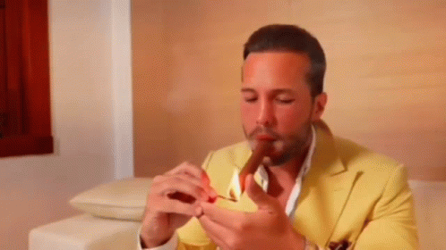 a man in a yellow suit is lighting a cigar with a match .