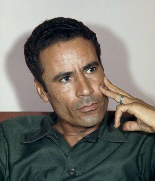 This may contain: a man in a green shirt is holding his finger to his temple's ear