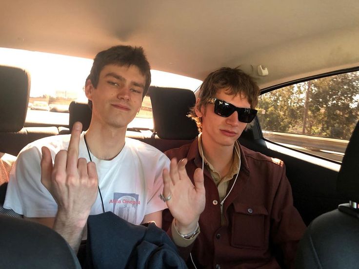 This may contain: two young men sitting in the back seat of a car with their hands raised up
