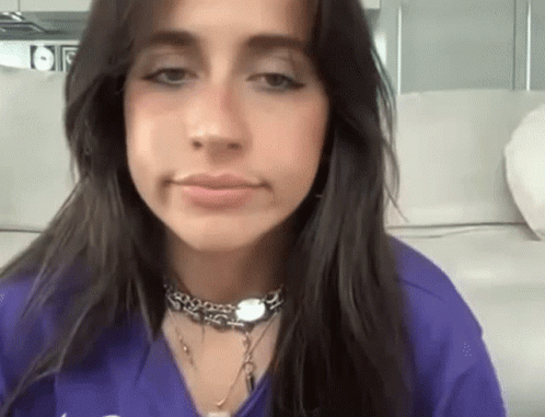 a woman with long dark hair is wearing a purple shirt and a necklace .