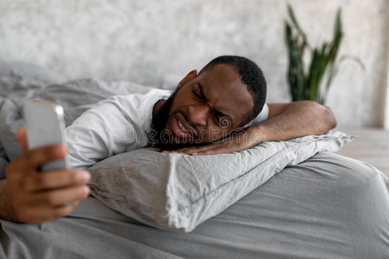 black-man-suffering-insomnia-looking-phone-bed-bad-news-oversleep-shocked-confused-wakes-up-anxiety-surprised-230651908.jpg