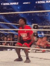 a man in a red shirt is kneeling in a wrestling ring while another man is laying on the ground .