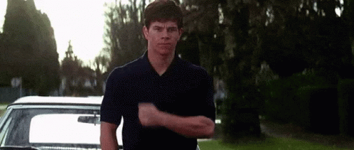 a man in a blue shirt is standing in front of a car and making a funny face .