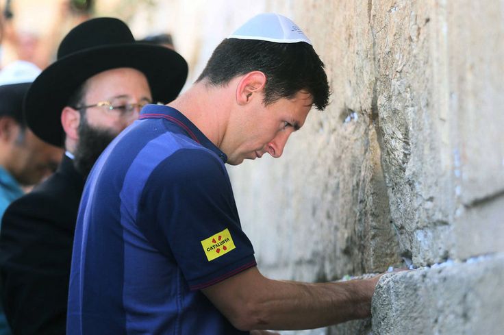 This may contain: a man wearing a blue shirt and hat leaning against a stone wall