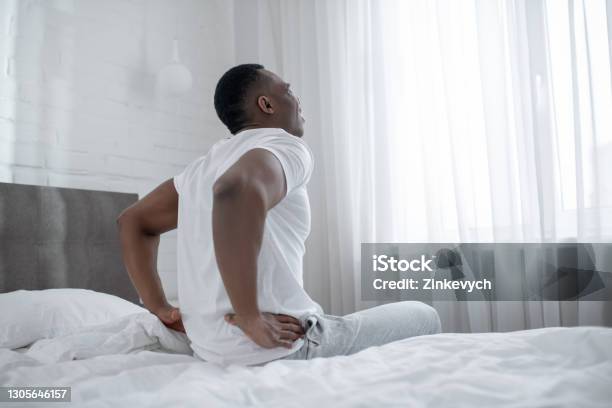 african-american-man-sitting-on-bed-and-touching-his-back.jpg