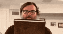 a man with a beard and glasses is holding a book in front of his face
