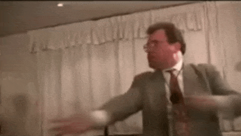a man in a suit and tie is dancing in front of white curtains .