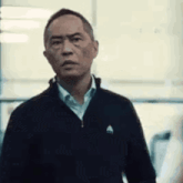 a man in a black jacket is standing in front of a window and looking at the camera .