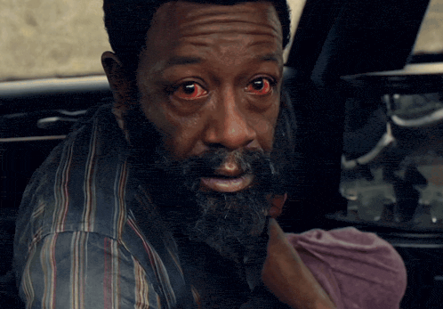 a man with red eyes and a beard looks at the camera