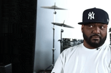 a man wearing a new york yankees hat is sitting in front of a drum set