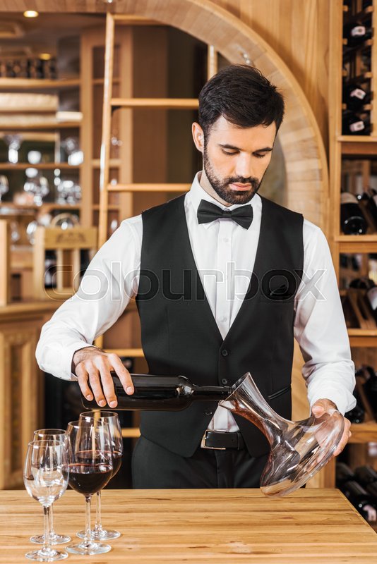 handsome young wine steward pouring wine into decanter at wine store |  Stock image | Colourbox