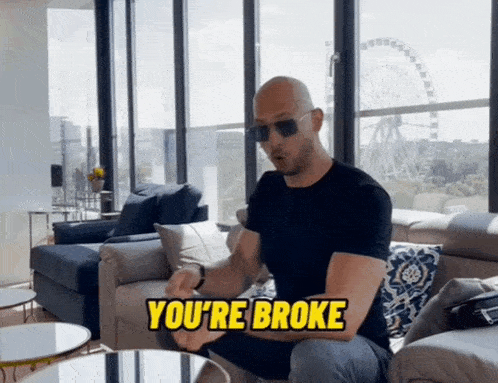 a bald man is sitting on a couch with the words you 're broke written above him