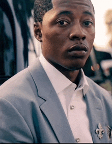 a man in a suit has a fleur de lis brooch on his jacket