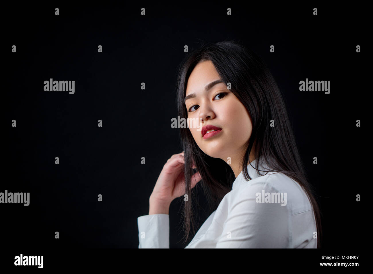 half-asian-attractive-woman-in-white-shirt-in-half-turn-looking-at-camera-against-black-background-MKHN0Y.jpg