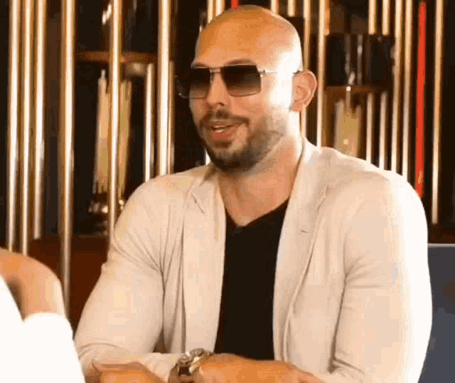 a bald man with a beard and sunglasses is sitting at a table .