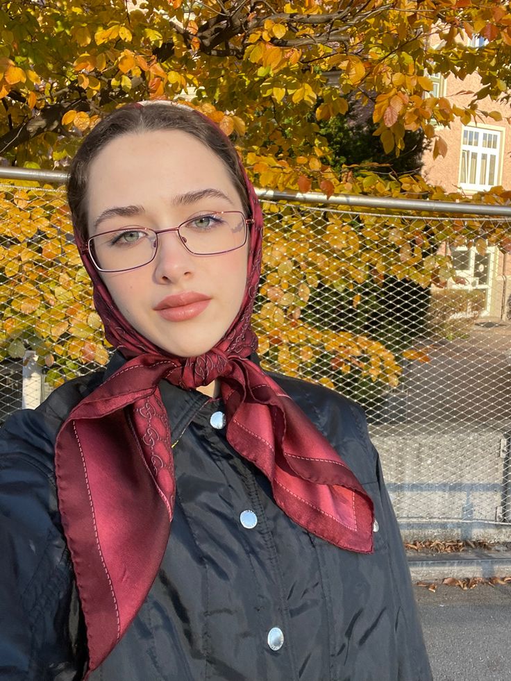 This contains: A girl in a red scarf making a selfie in front of a golden autumn tree