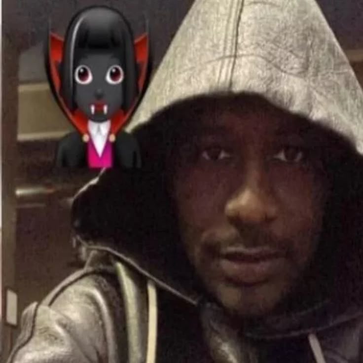 This may contain: a man wearing a hoodie with a black cat on top of his head in front of him