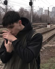 a young man standing in front of train tracks holding his hands to his face while looking at the camera a young man standing in front of train tracks holding his hands to his face while looking at the camera